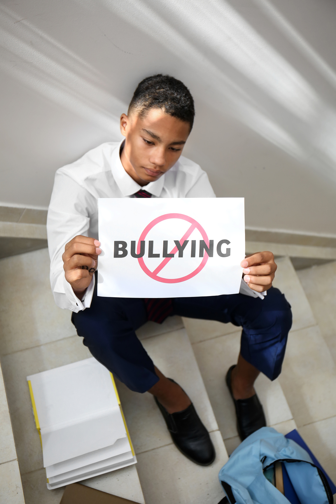 African-American Teenage Boy Holding Sheet of Paper with Word BULLYING at School